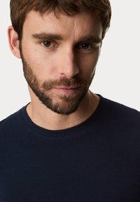 Marineblaue Baumwoll-T-Shirt mit Rundhalsausschnitt und kurzen Ärmeln, glatte Textur und einfache Stickdetails, getragen von einem männlichen Model.