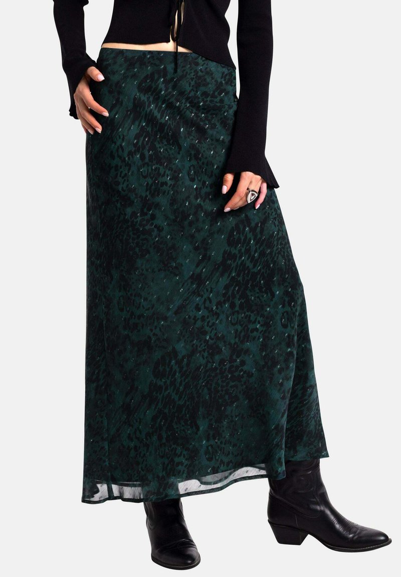 Una falda maxi en verde oscuro con un patrón de estampado animal texturizado. Material translúcido y un diseño fluido, combinada con botas de vaquero negras.