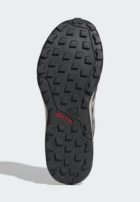 Suela de zapato de goma negra con superficie texturada, que presenta tacos triangulares y rectangulares para tracción, con la marca "TRACXION" en rojo.