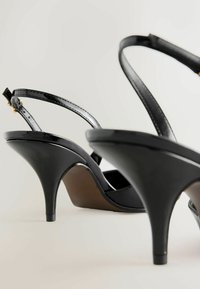 Melni augstpapēžu sandales ar spīdīgu apdari, regulējamām potīšu siksnām un elegantu dizainu. Papēdis izliecas augšup ar eleganci.