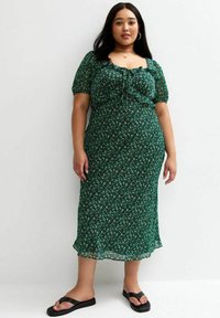 Groene bloemen-midi-jurk met pofmouwen, gerimpelde halslijn en vloeiend materiaal, gecombineerd met zwarte slippers.