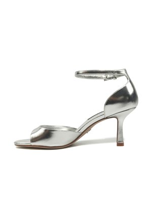 Sandale ouverte argent métallique avec bride à la cheville et talon fin de hauteur moyenne sur fond blanc.