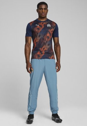 Blue athletic shirt with orange and black abstract pattern, paired with light blue pants, featuring elastic cuffs and logo accents.