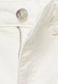 Bijele traperice s srebrnim patentnim zatvaračem i kopčom na dugme. Prikaz u blizini prikazuje glatku teksturu i detalje šivanja.