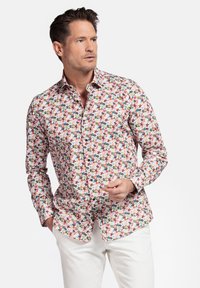 Chemise blanche à manches longues avec un motif floral coloré en rouge, bleu et vert, dotée d'un col, associée à un pantalon blanc.
