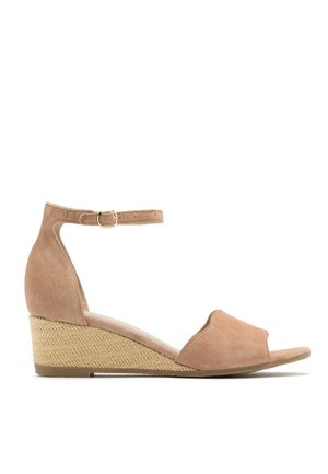 Sandał na koturnie z beżowego zamszu z paskiem wokół kostki, odkrytymi palcami i teksturowanym koturnem z juty. Prosta, gładka sylwetka z minimalistycznymi zdobieniami.