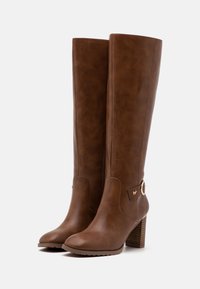 Botas marrones hasta la rodilla con un acabado de faux cuero suave, punta redondeada y detalles en tono dorado. Cuentan con un tacón de bloque texturizado.