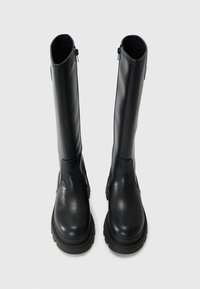 Botas de cuero negro hasta la rodilla hecha de cuero suave. Presenta una puntera redondeada, suela gruesa de plataforma y cremallera lateral para facilitar su uso.