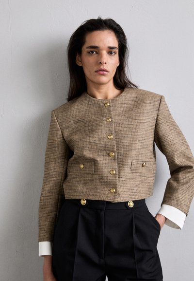 Bruin geruit cropped jasje met een ronde hals, gouden knopen en twee voorzakken. Afgewerkt met witte cuffs, gecombineerd met zwarte broeken.