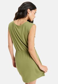 Vestido corto verde de manga corta con un corte relajado, cinturilla elástica y textura suave, con un escote en la espalda y un diseño minimalista.