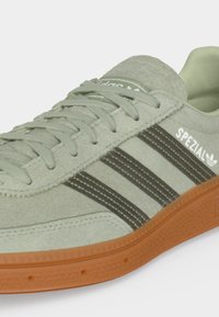 Ανοιχτό πράσινο παπούτσι Adidas Spezial με σκουροπράσινες ρίγες και καουτσούκ σόλα σε λευκό φόντο.