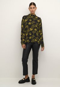 Maglietta nera a maniche lunghe con motivo floreale giallo; design a collo alto. Abbinata a pantaloni neri in finta pelle attillati e mocassini neri.