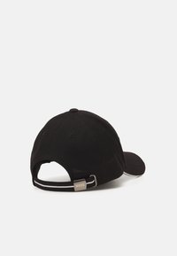 Schwarze Baseballmütze aus Mesh-Stoff, mit gebogenem Schirm, verstellbarem Riemen und einem Logosticker auf der Rückseite. Strukturierte und leichte Ausführung.