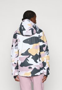 Mitmevärviline veekindel jakk, millel on kamoflaažimuster roosa, musta ja kollase varjunditega, varustatud kapuutsi ja elastsete mansettidega.