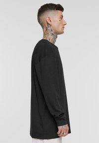Svart langermet t-skjorte utstilt. Har rund hals, avslappet passform, ribbede mansjetter og glatt bomullsstoff. Enkel design, ingen mønstre eller aksenter.