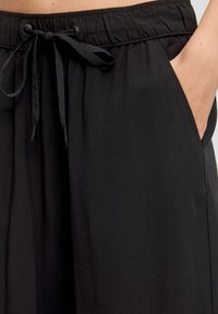 Zwarte shorts met elastische tailleband, trekkoord en twee zijzakken. Glad stoftextuur en ontspannen pasvorm ontwerp.