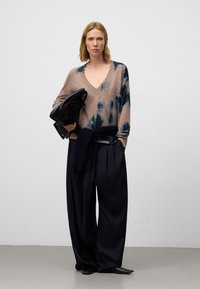 Pull beige et bleu marine tie-dye avec un col en V, associé à un pantalon bleu marine ample, agrémenté d'un sac noir texturé et d'un accent tricoté.