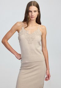 Beige gebreide tanktop met kant als afwerking langs de halslijn. Voorzien van dunne bandjes en een getailleerd ontwerp, gecombineerd met een bijpassende rok.