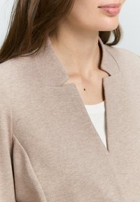 Blazer in tessuto beige e texture con colletto a ripiego e scollatura a V profonda. Vestibilità aderente con delicate righe verticali.