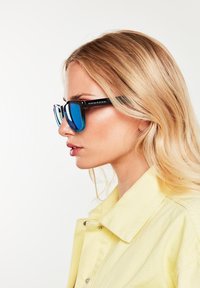 Ochelari de soare negri și albaștri cu o formă rectangulară și lentile reflectorizante, având un design îndrăzneț și logo-ul "HAWKERS" pe braț.