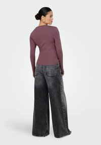 Maglietta a maniche lunghe color malva con design aderente abbinata a jeans neri a vita alta e gamba larga con una texture denim sbiadita e cuciture visibili.