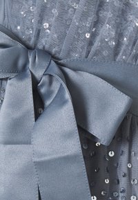 Tessuto in rete grigio impreziosito da paillettes con un nastro di raso annodato. Il materiale ha una texture trasparente con dettagli riflettenti sparsi.