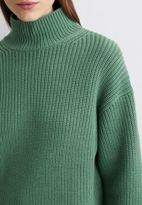 Grüner, gerippter Rollkragenpullover in lässigem Schnitt. Er zeichnet sich durch ein dickes, strukturiertes Muster und weite, lässige Ärmel aus.