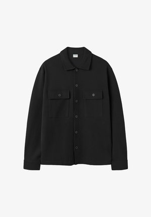 Musta napillinen paita, valmistettu sileästä kankaasta, jossa on avokaulus, kaksi etutaskua ja pitkät hihat napitettavilla kalvosimilla.