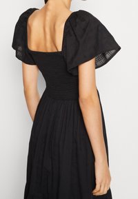 Schwarzes Kleid mit kurzen, puffigen Ärmeln und einem quadratischen Ausschnitt. Das Oberteil hat eine Raffung, und der Rock hat ein fließendes, plissiertes Design.