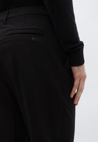 Čierne nohavice s hladkou tkaninou, strihaným dizajnom a elegantným zadným vreckom s reliéfnou značkou. Zvýraznené priliehavým pásom.