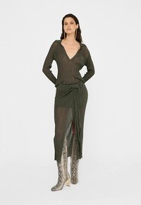 Olivengroene gebreide top met V-hals en lange mouwen, gecombineerd met een bijpassende wikkelrok met een hoge split. Zilverkleurige kniehoogte laarzen met slangenprint.