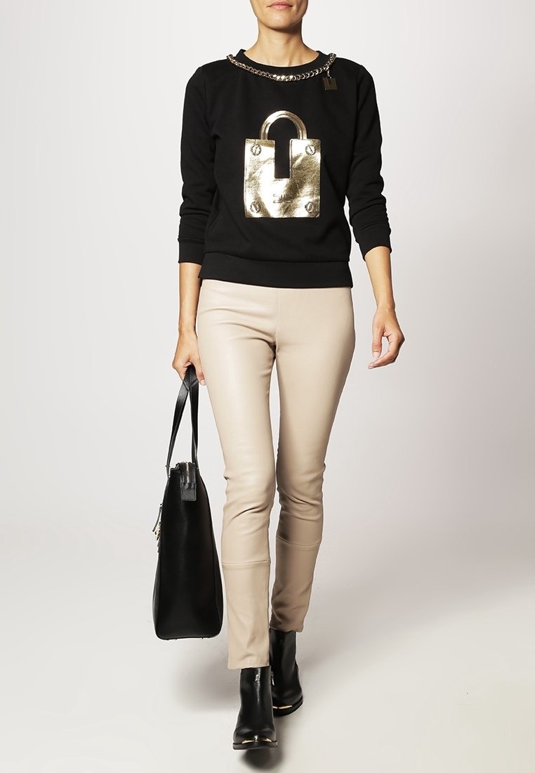 Sweatshirt noir avec design de cadenas métallique, pantalon beige ajusté, sac noir et bottines. Détail en chaîne au niveau du col. Textures lisses.