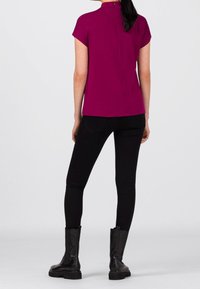Fuchsia kortærmet top med høj hals og lynlås i ryggen, parret med sorte skinny jeans og sorte ankelstøvler. Enkel, stilren design.