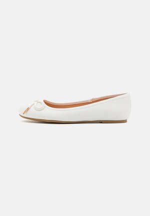 White ballet flat features a smooth texture, round toe, and a small gold-accented loop detail on the front. Light brown sole.