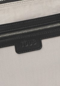 Czarny skórzany zamek błyskawiczny z srebrnymi okuciami na jasnoszarym, teksturowanym tle tkaniny, z tłoczonym logo.