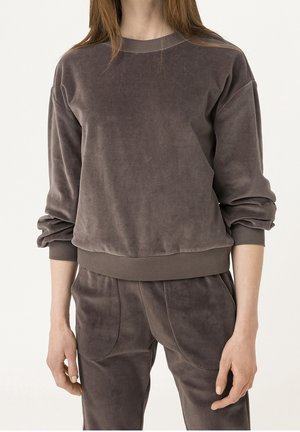 Kobieta ubrana w brudnoróżową welurową bluzę z długim rękawem oraz dopasowane welurowe spodnie z wysokim stanem i elastycznym paskiem.