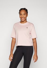 Camiseta cropped rosa-claro com mangas curtas e decote redondo. Apresenta um pequeno logótipo triangular no peito. Tecido de algodão suave.