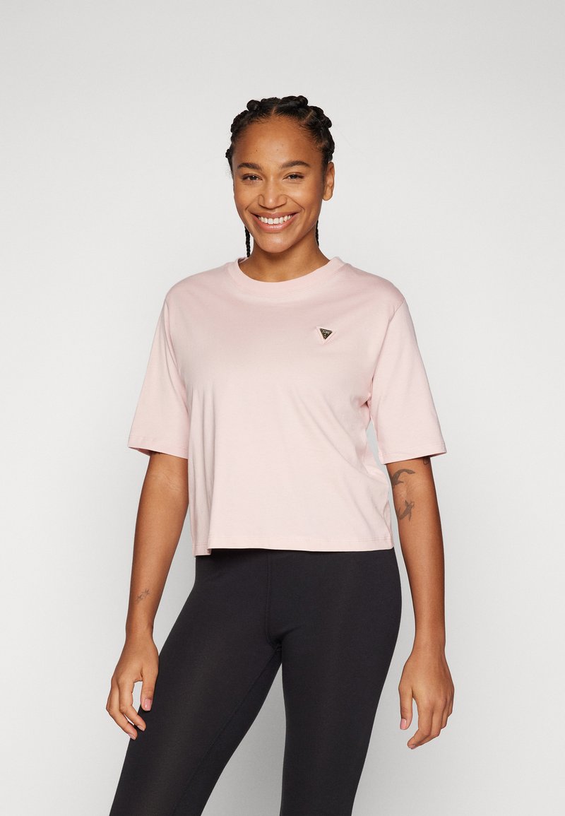 Camiseta cropped rosa-claro com mangas curtas e decote redondo. Apresenta um pequeno logótipo triangular no peito. Tecido de algodão suave.