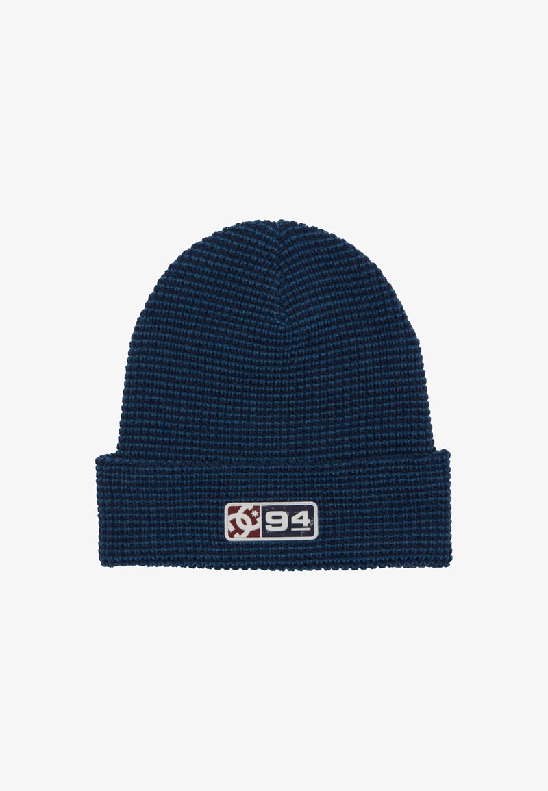 Bonnet en tricot bleu marine avec motif texturé, doté d'un revers replié et d'une étiquette rectangulaire arborant un logo et le chiffre "94" en couleurs contrastées.