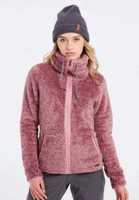 Giacca in pile rosa e morbido con colletto alto, due tasche frontali e zip frontale. Abbinata a un berretto in maglia scura con un'etichetta del logo.