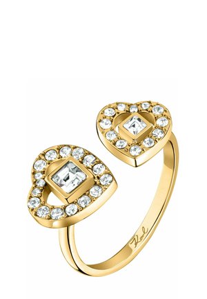 Anello d’oro con due estremità a forma di cuore, ciascuna con un cristallo quadrato al centro circondato da cristalli rotondi più piccoli.