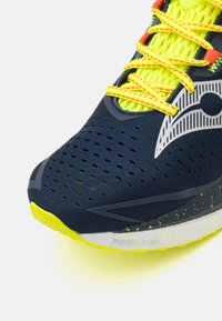 Mornarske sportske cipele s mrežastim gornjim dijelom i neon žutim naglascima. Imaju teksturiranu površinu i uzorak na đonu za bolju prijanjanje i potporu.