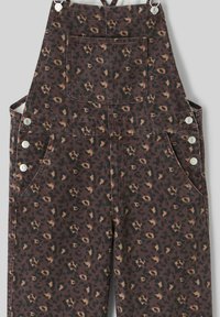 Salopette en velours côtelé marron avec un motif léopard. Dotée de garnitures argentées, de poches latérales et d'une poche frontale. Tissu texturé.