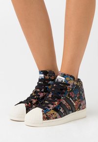 Hoge sneakers met een meerkleurig mesh ontwerp, zwarte veters en een witte rubberen neuskap. Branding zichtbaar op de tong en zijkant.