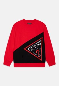 Rode en zwarte sweatshirt met lange mouwen, voorzien van een groot driehoekig GUESS-logo op de voorkant, met witte en rode tekst en symbolen.