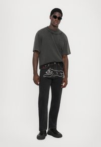 Svarte denimjeans med perlepynt og en svart bomull T-skjorte med plisserte detaljer. Komplimentert med svarte solbriller og sko.