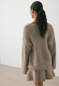 Bruine gebreide trui met een losse pasvorm en geribbelde textuur, gecombineerd met een bijpassende flare rok. Zacht, fuzzy materiaal en een casual design.