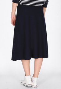 Marineblaue A-Linien-Rock aus leichtem Stoff, mit glatter Textur und einem Saum, der knapp unter dem Knie sitzt, kombiniert mit weißen High-Top-Sneakern.