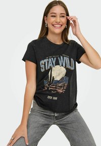 Zwarte katoenen t-shirt met een grafisch ontwerp dat de tekst "STAY WILD" en een woestijnlandschap bevat, met korte mouwen en een ronde hals.