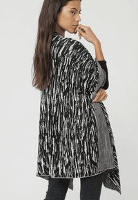 Chale de patrón en blanco y negro con un diseño suelto y drapeado. La tela parece ligera con una textura suave y un detalle de dobladillo en contraste.